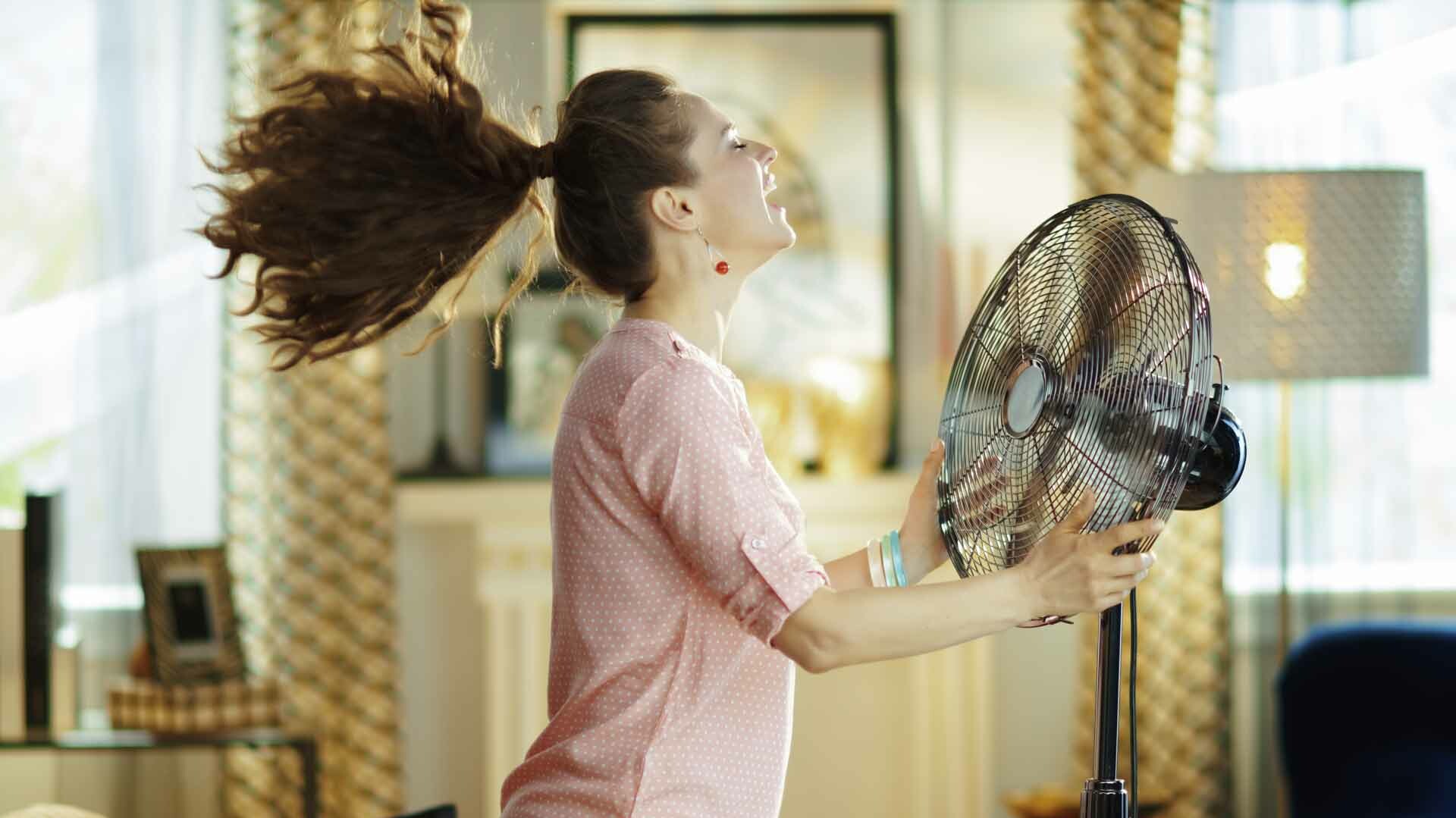 Frau steht vor Ventilator, die Haare wehen