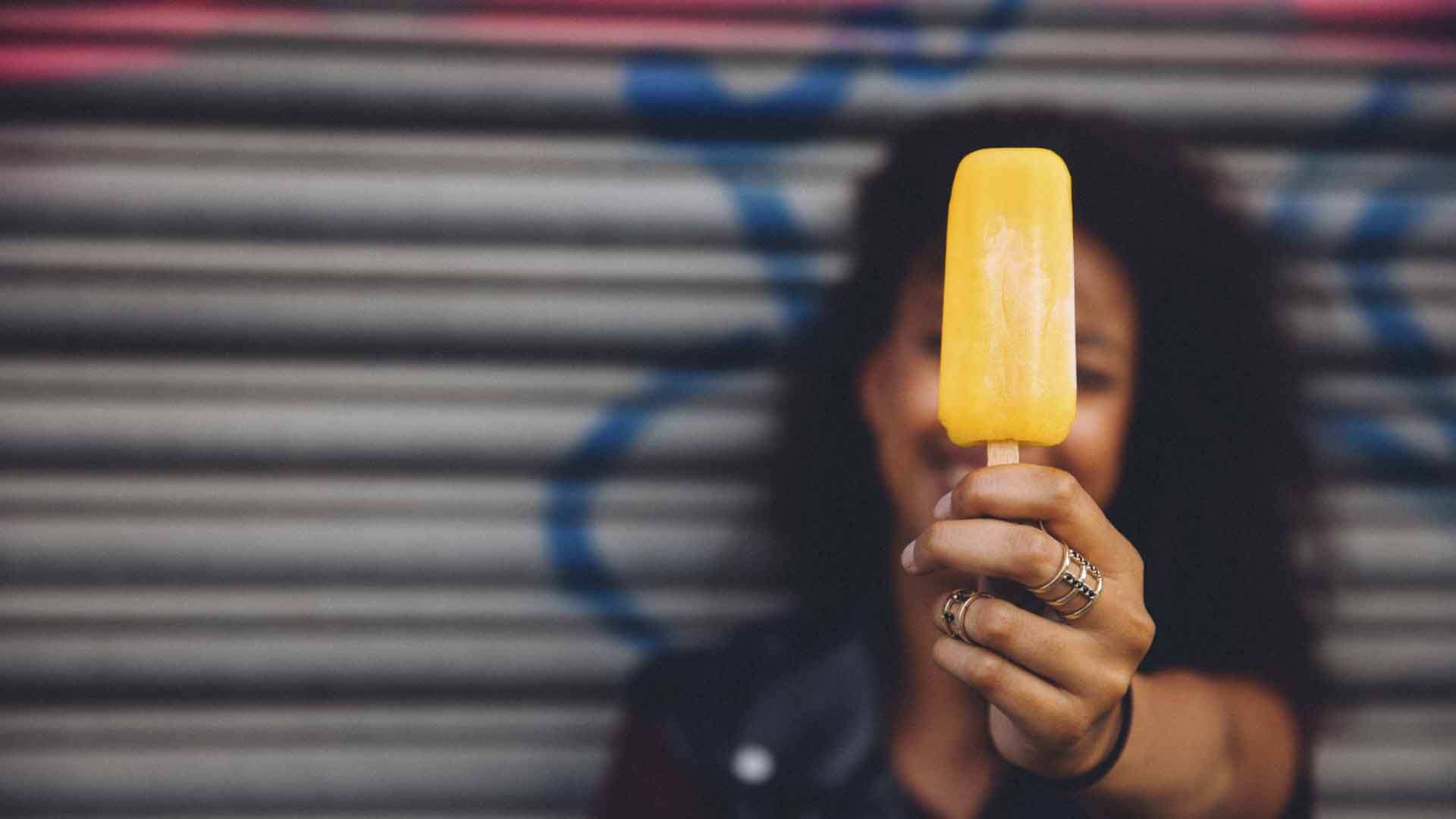 Frau hält ein gelbes Eis ins Bild